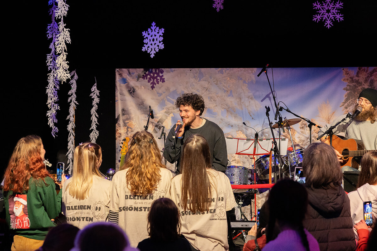 Sänger Tilmann bei dem Winterspektakel vor einer Gruppe Menschen auf der Bühne, er singt und lächelt dabei.